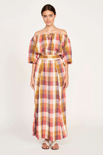 Model wearing a fashionable plaid off-shoulder top and matching long skirt, styled for a chic summer look.